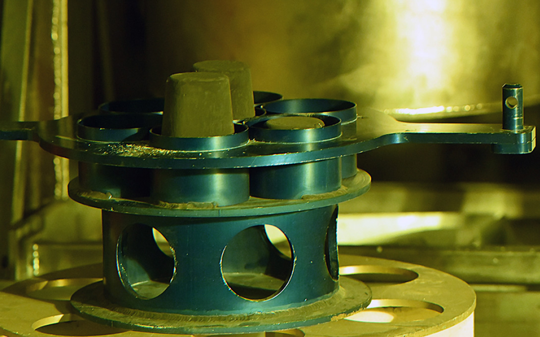 Grey high-assay low-enriched uranium cylinders in metallic form in a green holder.