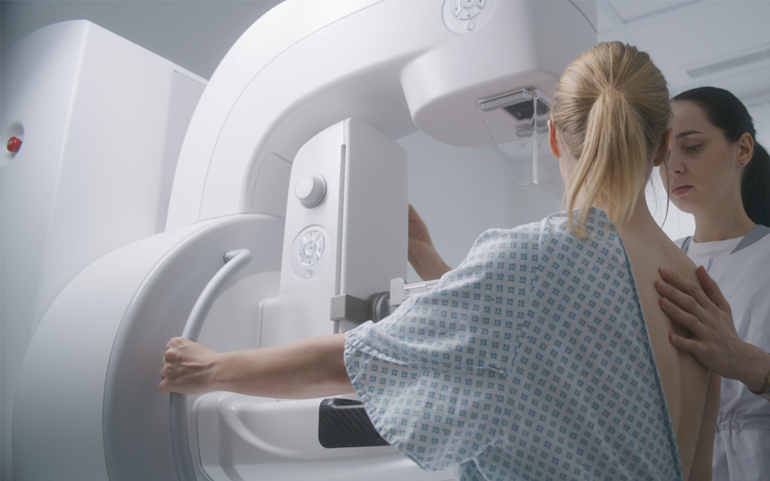 Woman shown getting a mammogram with technician standing by her
