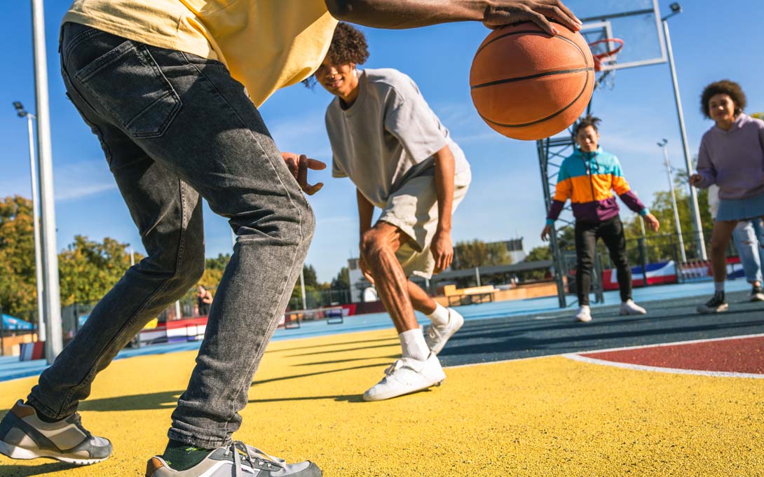 Multiracial group of young friends bonding outdoors and having fun playing  basketball
