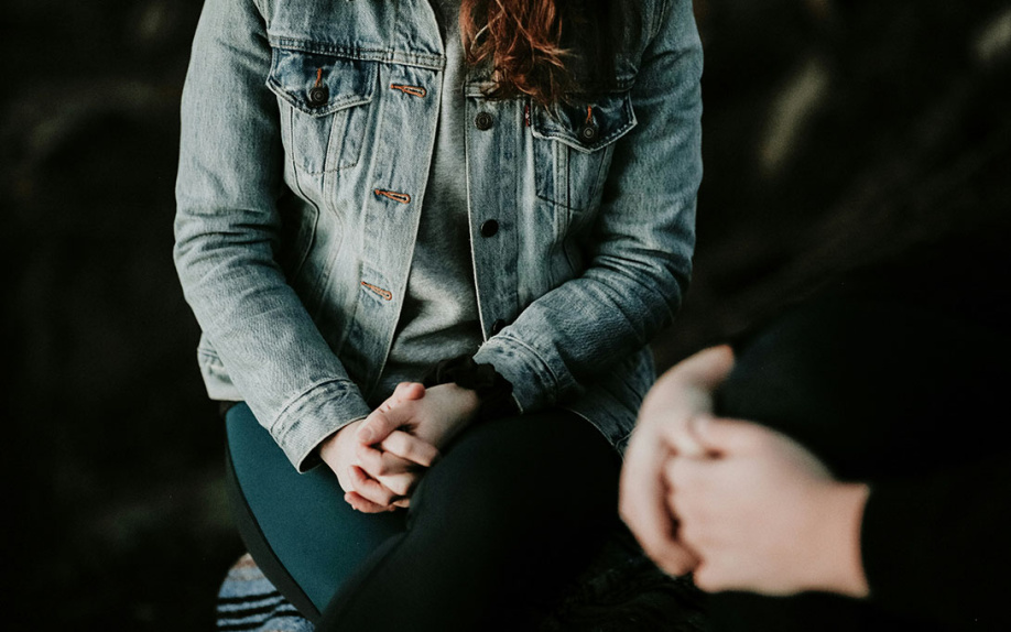 Two figures seated with just clasped hands showing like part of a support group