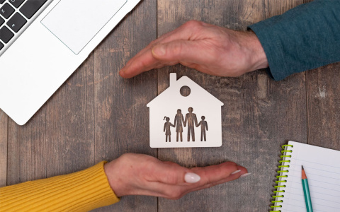 Computer, two hands holding drawing with house with people in it