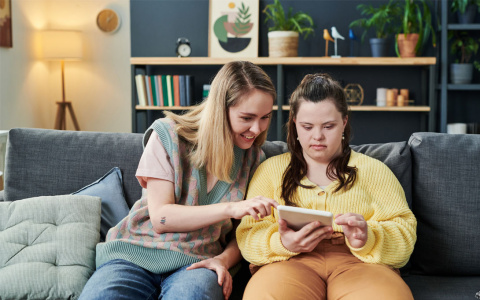 caregiver helps young woman with Down's syndrome use an ipad
